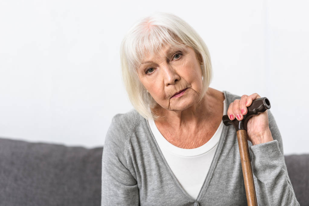 Nachdenkliche Seniorin mit Holzstock blickt in Kamera - Foto, Bild