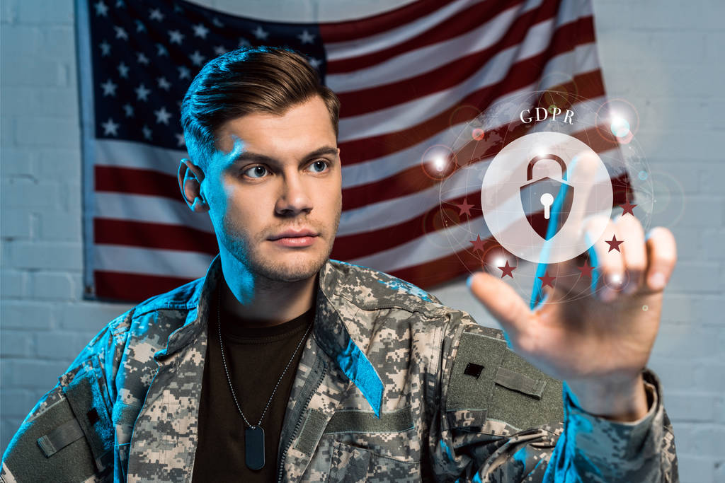 επιλεκτική εστίαση του όμορφου στρατιώτη που σημαδεύει με το δάχτυλο στο λουκέτο κοντά στην αμερικάνικη σημαία  - Φωτογραφία, εικόνα