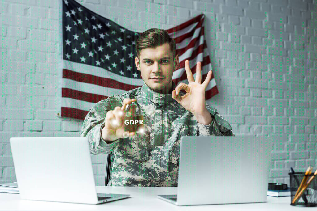 man in military uniform holding padlock with gdpr lettering near laptops and showing ok sign  - Photo, Image