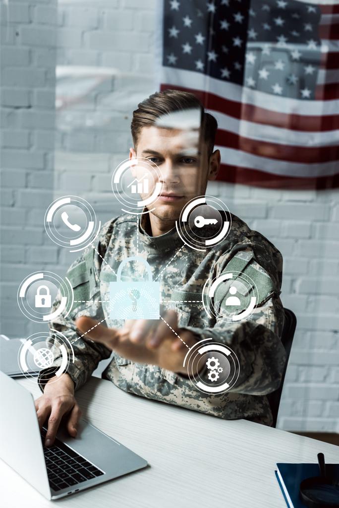 schöner Soldat in Militäruniform, der mit dem Finger auf virtuelles Vorhängeschloss zeigt, während er Laptop benutzt  - Foto, Bild