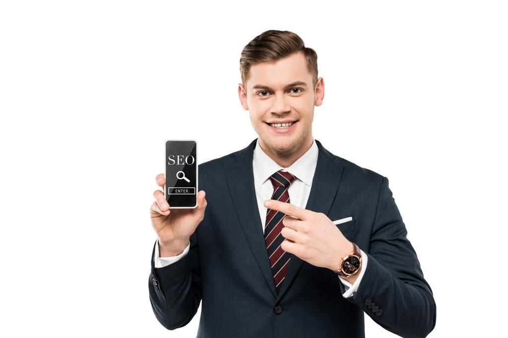 gelukkige zakenman in pak wijzend met de vinger op de smartphone met SEO belettering op het scherm geïsoleerd op wit  - Foto, afbeelding