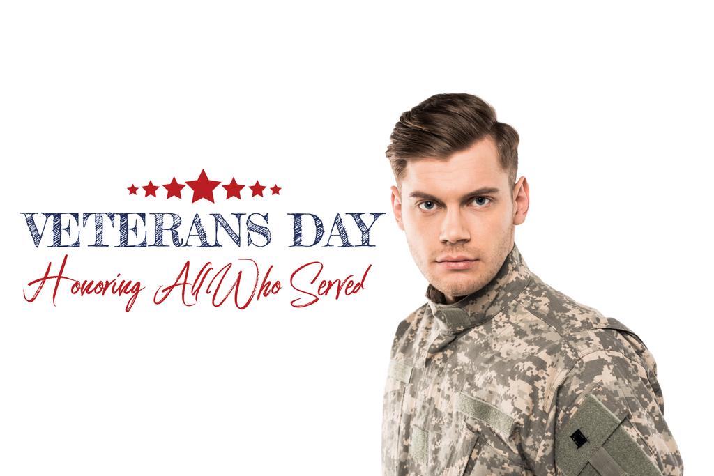 serious and handsome soldier in uniform looking at camera near veterans day lettering on white  - Photo, Image