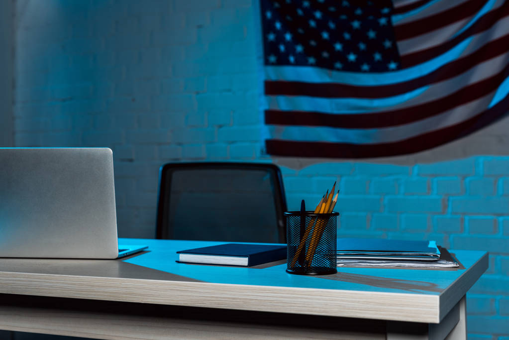 laptop near stationery on table near american flag in modern office  - Photo, Image