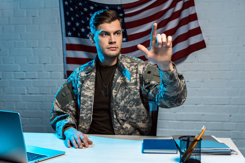 schöner Soldat in Uniform sitzt neben Laptop und gestikuliert im Büro  - Foto, Bild