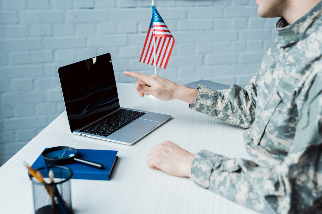 bijgesneden weergave van militaire man wijzend met de vinger op de laptop met blanco scherm  - Foto, afbeelding