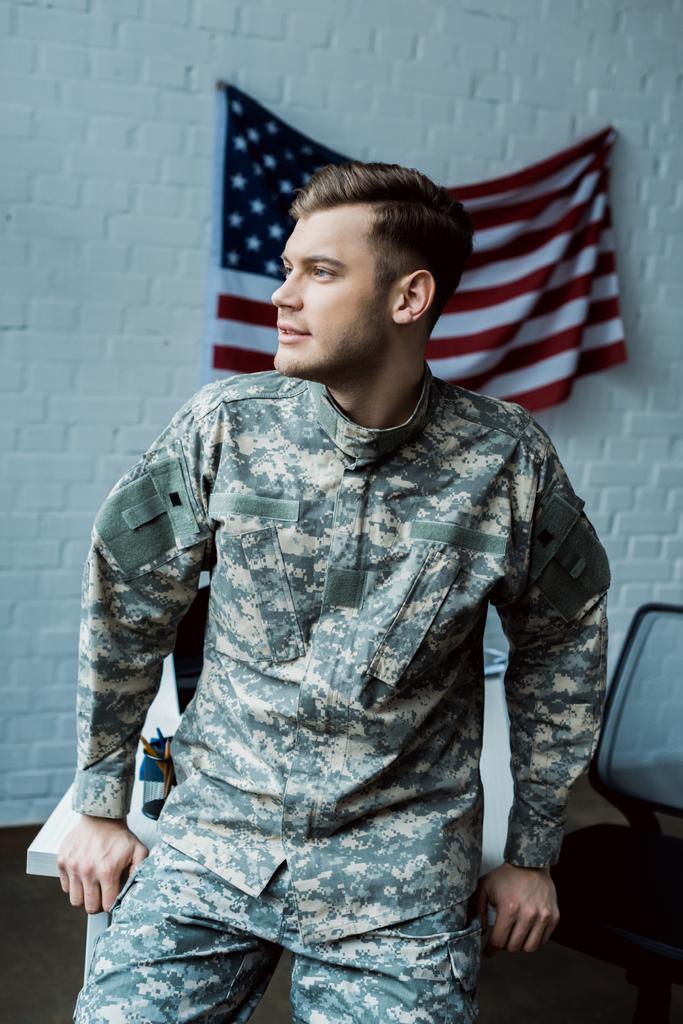knappe man in militair uniform staande in Office in de buurt van de Amerikaanse vlag  - Foto, afbeelding