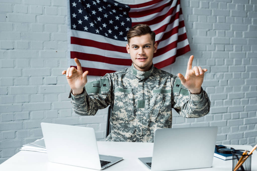 szczęśliwy żołnierz w mundurze ciężarnych w pobliżu laptopów w biurze  - Zdjęcie, obraz