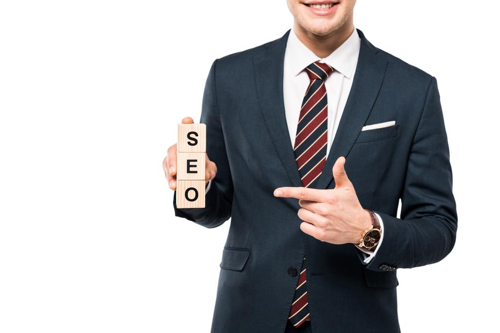 обрезанный вид веселый бизнесмен указывая пальцем на деревянные кубики с seo буквы изолированы на белом
  - Фото, изображение