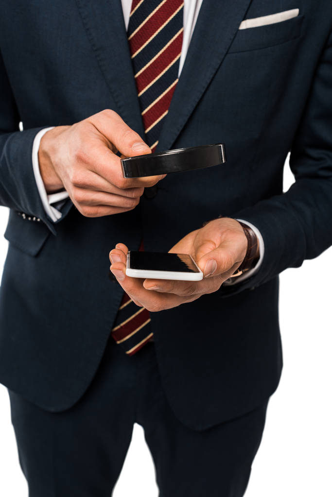 vista cortada de homem de negócios em terno segurando lupa perto de smartphone isolado no branco
  - Foto, Imagem