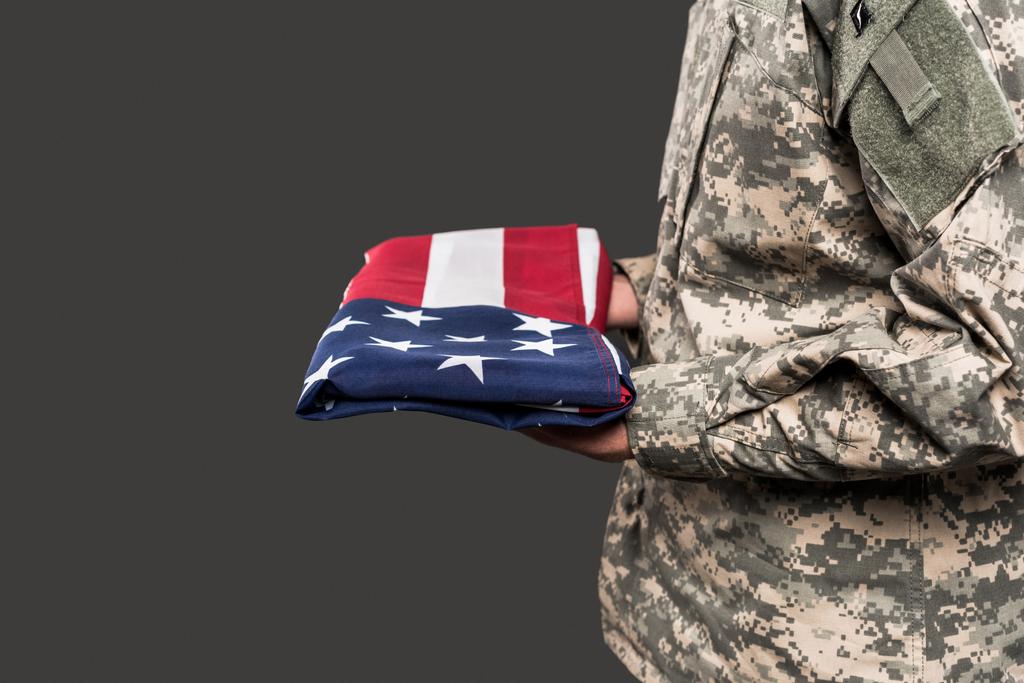 bijgesneden beeld van de mens in militaire uniform Holding vlag van Amerika geïsoleerd op grijs  - Foto, afbeelding
