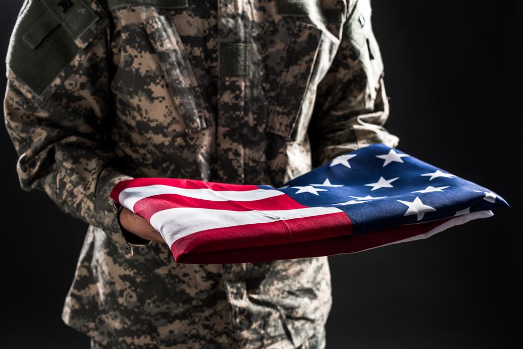 vista recortada del hombre en uniforme militar sosteniendo bandera de América aislado en negro
 - Foto, imagen