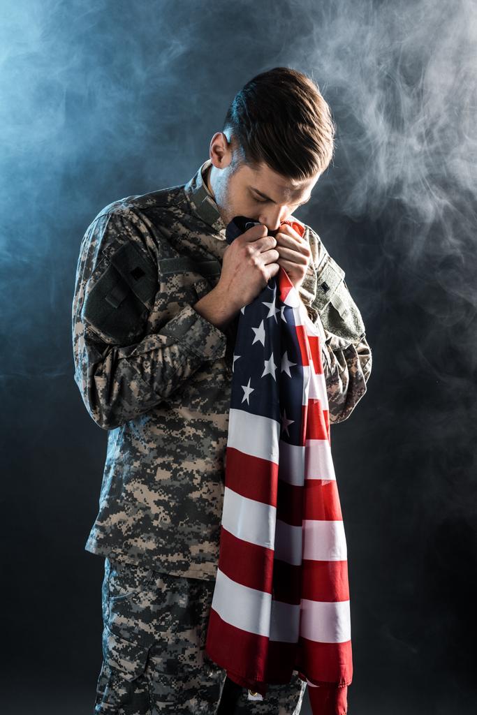 handsome soldier with closed eyes smelling american flag on black with smoke  - Photo, Image