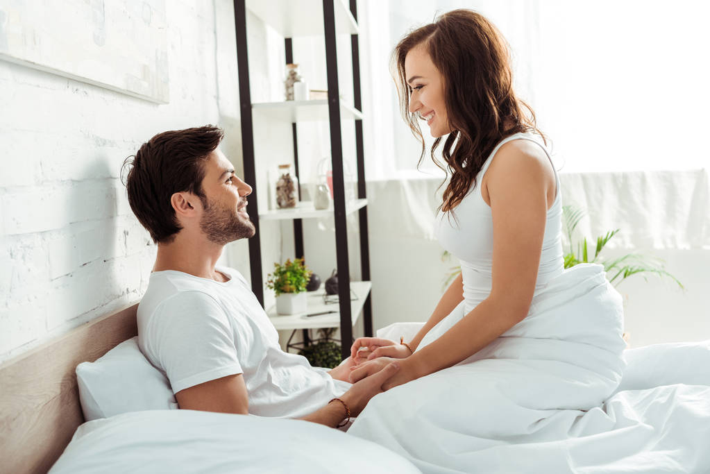 Gelukkig jonge vrouw kijken naar vriendje terwijl zittend op bed  - Foto, afbeelding