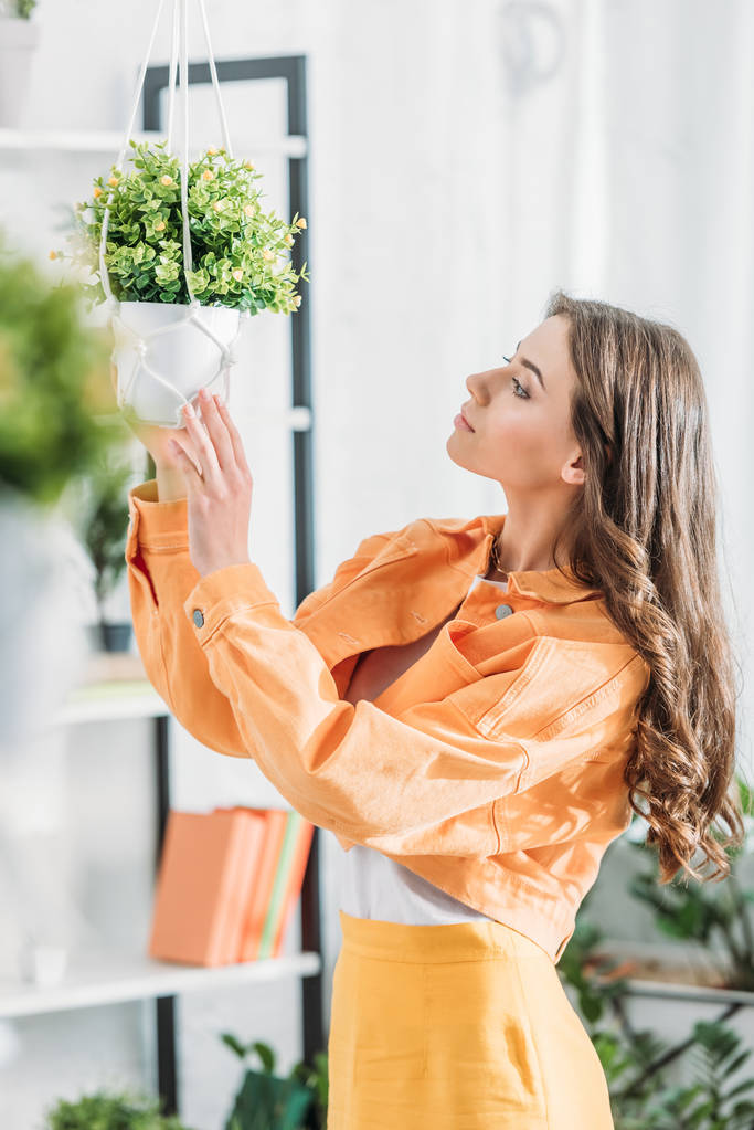 selective focus of pensive beautiful woman in orange clothing  touching flowerpot - Photo, Image