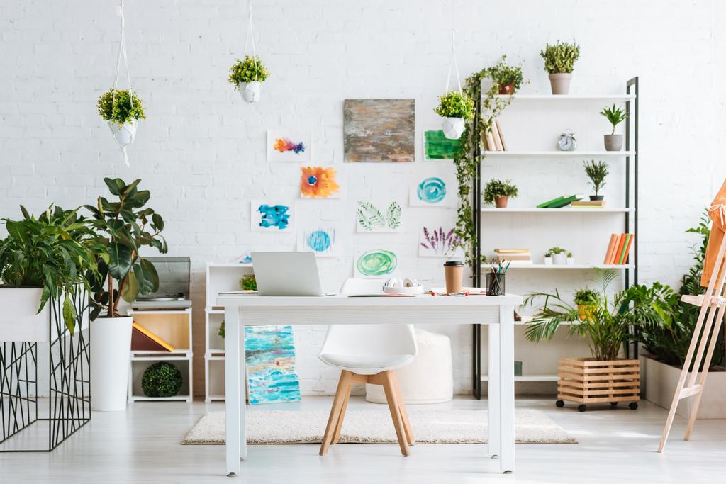 spacious room with desk, chair, rack, green potted plants and painting on white wall - Photo, Image