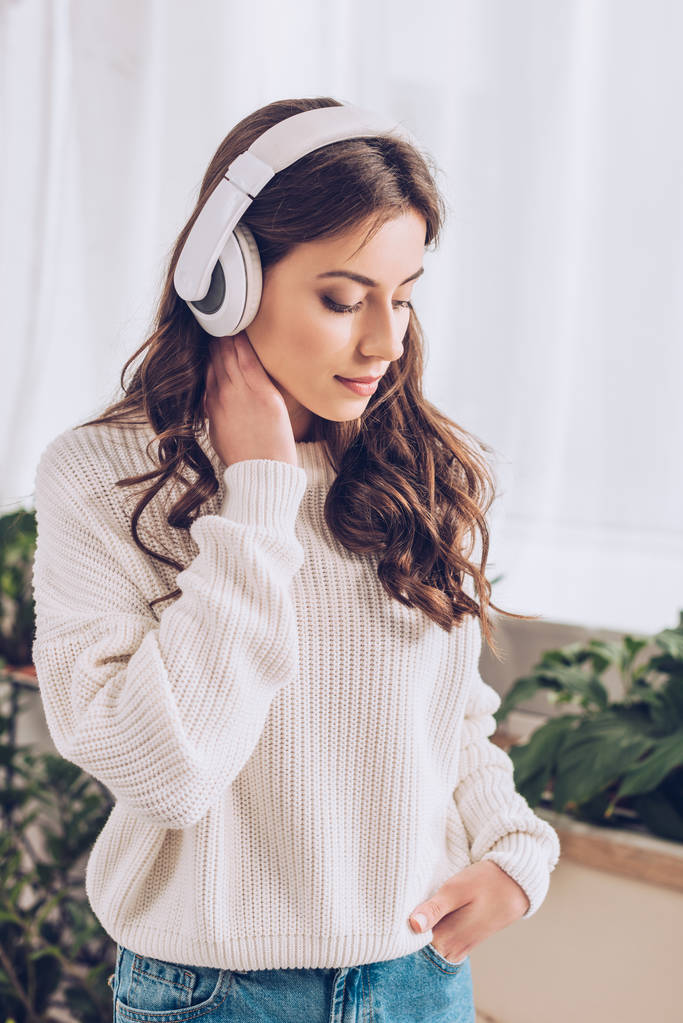 muchacha joven pensativa escuchando música en auriculares, tomados de la mano en el bolsillo y mirando hacia abajo
 - Foto, Imagen