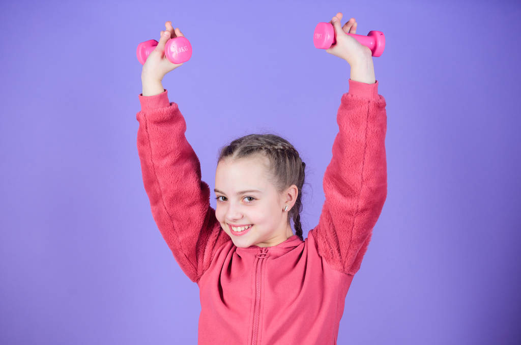 Счастливого детского спортсмена с гантелями. Тренировка маленькой девочки держать гантели. тяжелая атлетика для мускулов. Детская активность. Фитнес-диета для здоровья энергии. Спортивный успех. Упражнения с гантелями - Фото, изображение