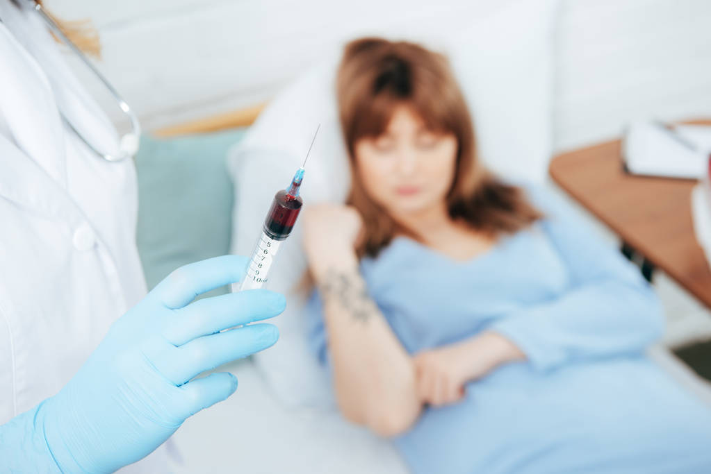 vue recadrée du médecin tenant la seringue avec échantillon de sang et donneur couché sur le lit
  - Photo, image