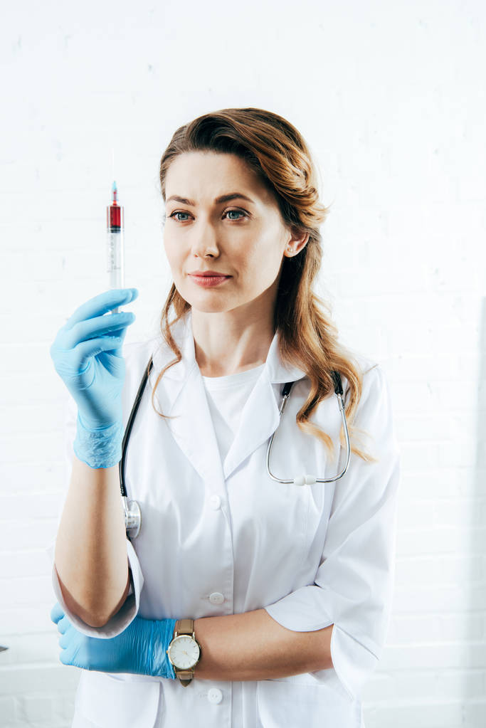 лікар в латексних рукавичках тримає шприц із зразком крові
 - Фото, зображення