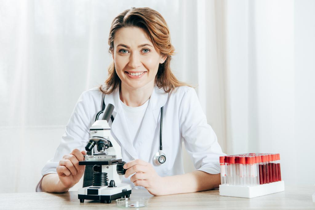 médico em casaco branco com estetoscópio usando microscópio na clínica
 - Foto, Imagem