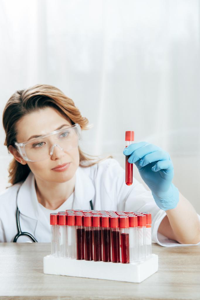 concentrated doctor in protective goggles holding test tube with blood - Photo, Image