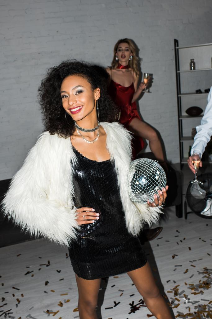 enfoque selectivo de la chica afroamericana feliz sosteniendo bola disco mientras está cerca de amigos
  - Foto, Imagen