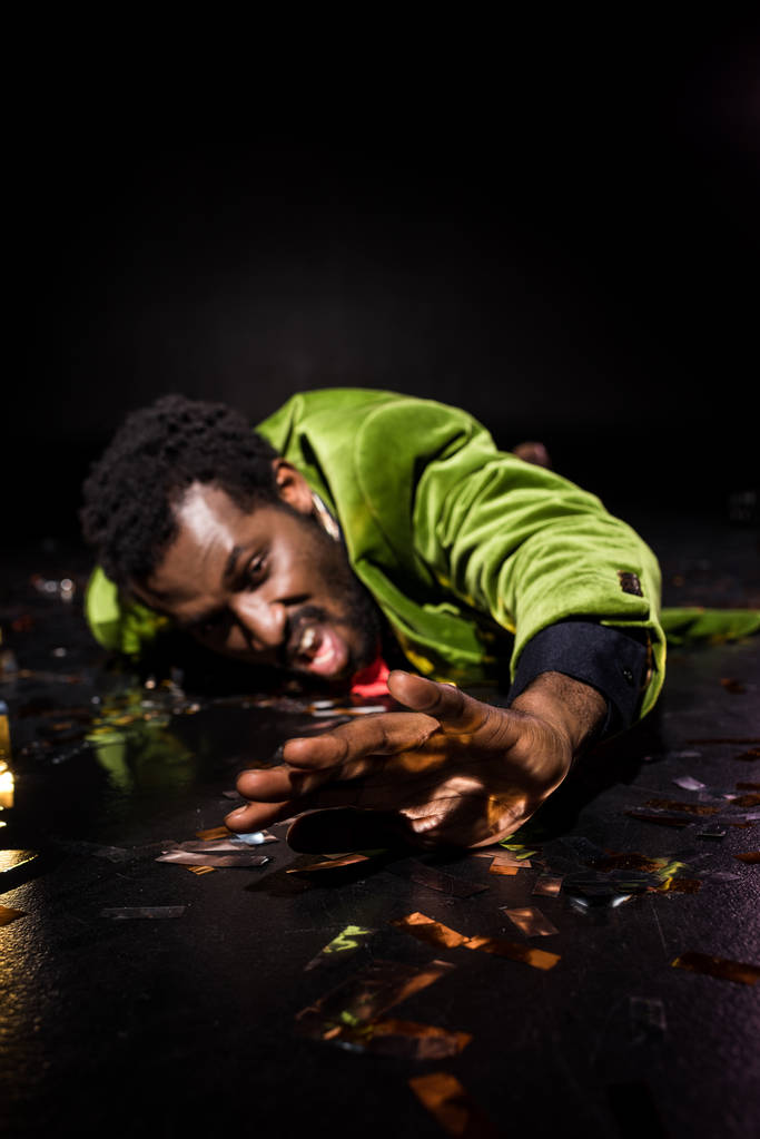 вибірковий фокус п'яного афроамериканця, що лежить на підлозі з блискучою конфетті на чорному
  - Фото, зображення