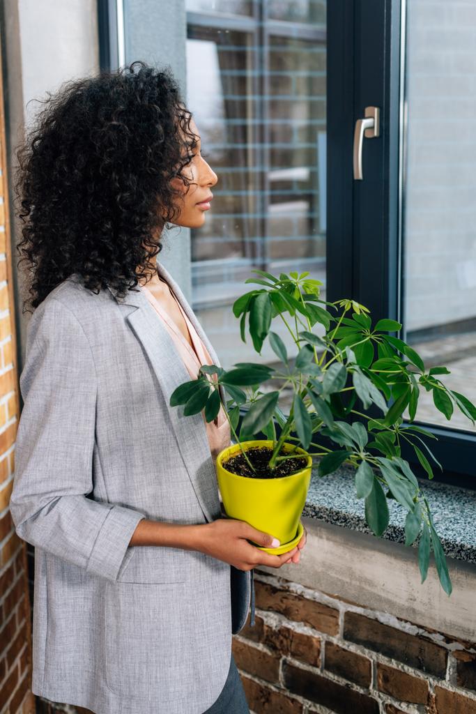 Αφρικανική αμερικανική περιστασιακή επιχειρηματίας κρατώντας γλάστρα με φυτό στο γραφείο σοφίτα - Φωτογραφία, εικόνα
