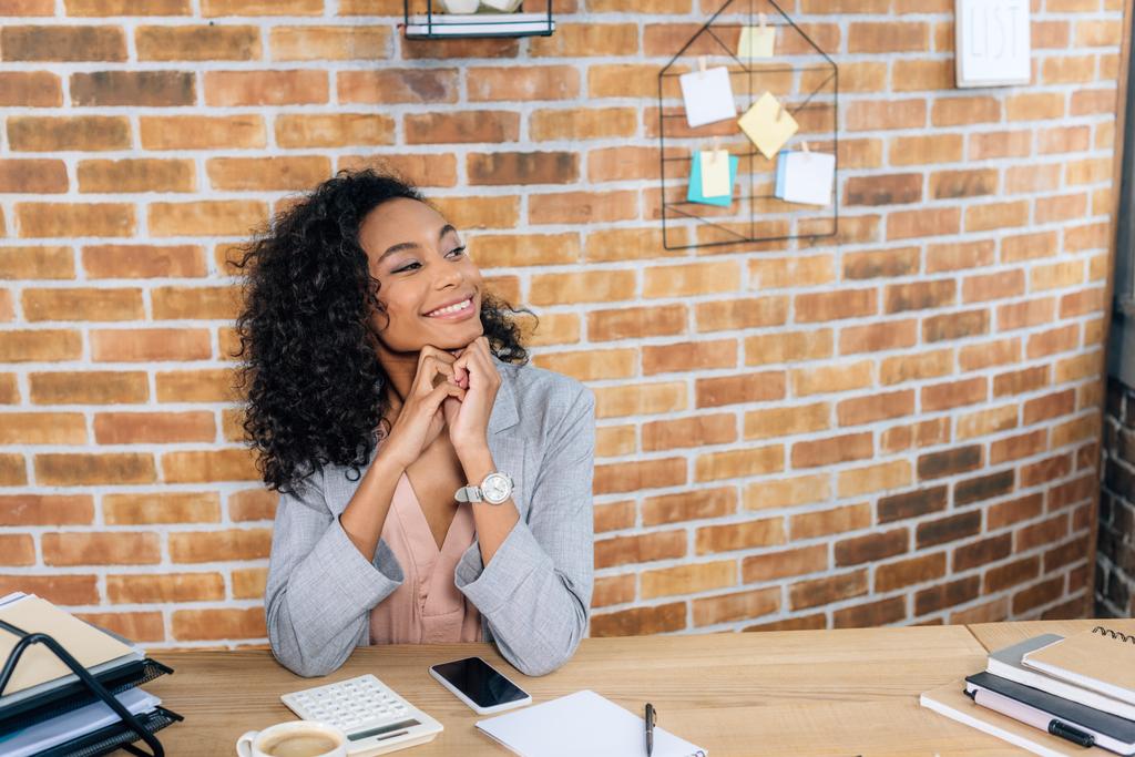 mooie lachende casual African American zakenvrouw zittend op tafel in Loft Office - Foto, afbeelding