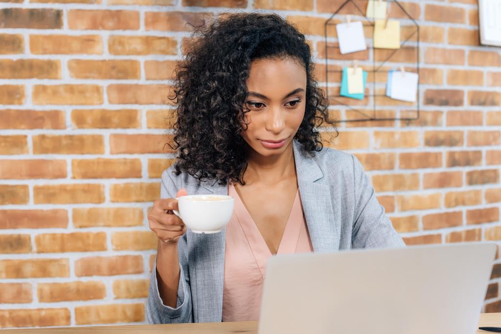 African American casual bizneswoman z filiżanką kawy za pomocą laptopa w biurze - Zdjęcie, obraz