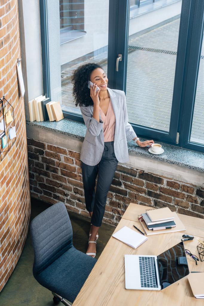 High-Winkel-Ansicht der schönen afrikanisch-amerikanischen Gelegenheitsunternehmerin im Gespräch auf dem Smartphone im Büro - Foto, Bild