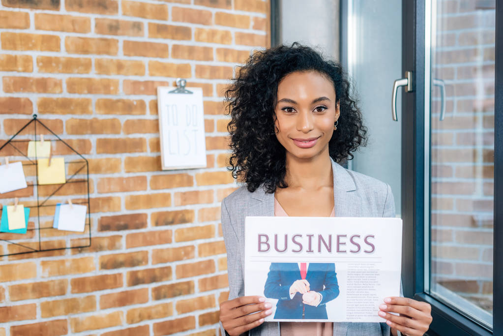 piękna Afrykańska amerykańska dorywczo bizneswoman Holding gazeta biznesowa w biurze Loft - Zdjęcie, obraz