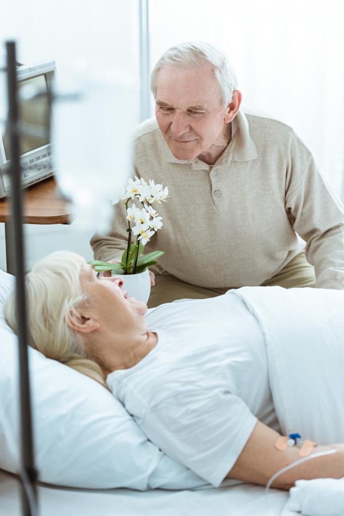 χαμογελαστή άρρωστη ηλικιωμένη γυναίκα που κοιτάζει τον σύζυγο στην κλινική - Φωτογραφία, εικόνα