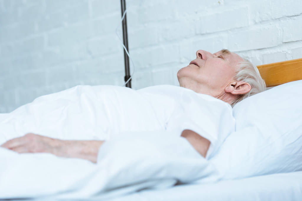 ανώτερος άνθρωπος σε κώμα ξαπλωμένο στο κρεβάτι στην κλινική - Φωτογραφία, εικόνα