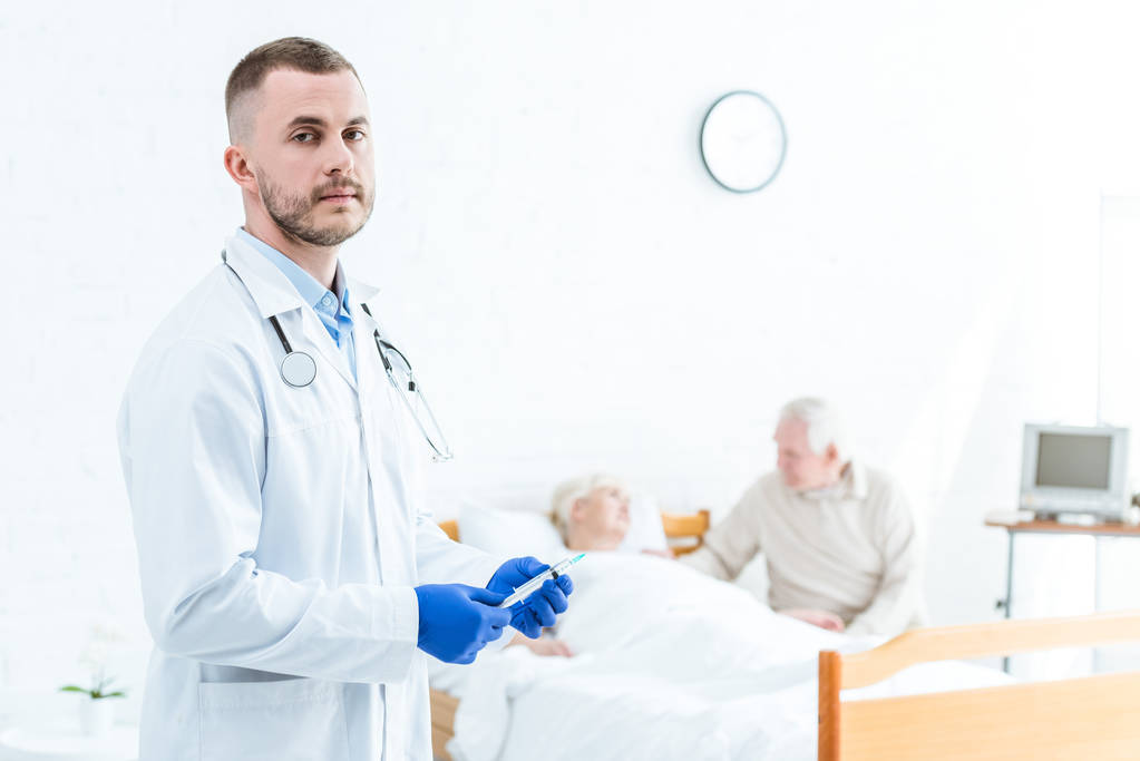 lekarz w rękawicach lateksowych trzymając strzykawkę, chory pacjent i starszy mężczyzna w klinice - Zdjęcie, obraz