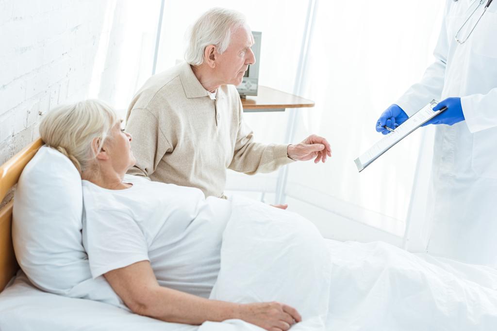 částečný pohled na lékaře držící schránku, nemocného pacienta a staršího muže na klinice - Fotografie, Obrázek