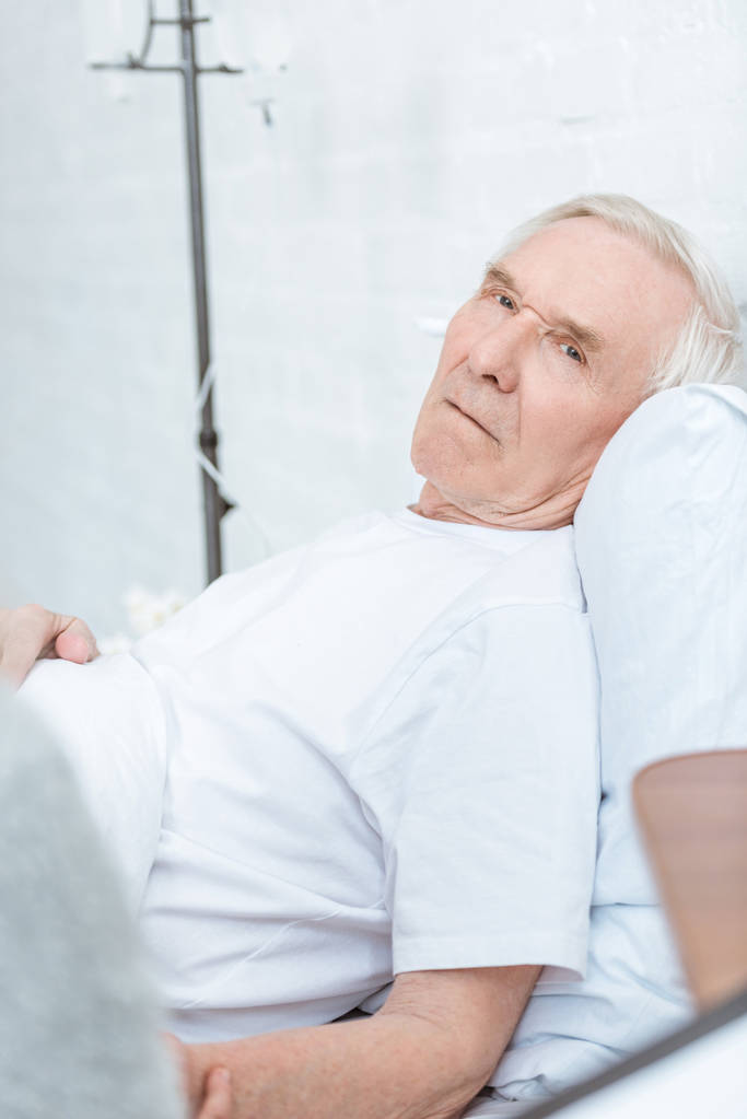 Kranker Senior liegt auf Bett und blickt in Klinik in Kamera - Foto, Bild