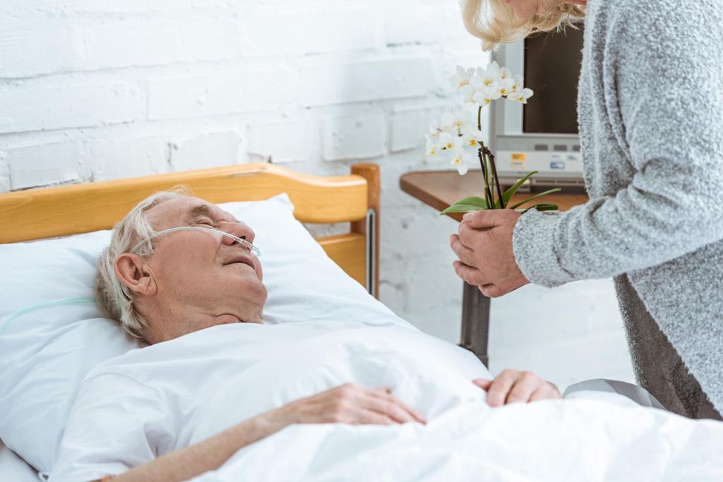 обрезанный вид пожилой женщины с орхидеями и больным пациентом в больнице
 - Фото, изображение