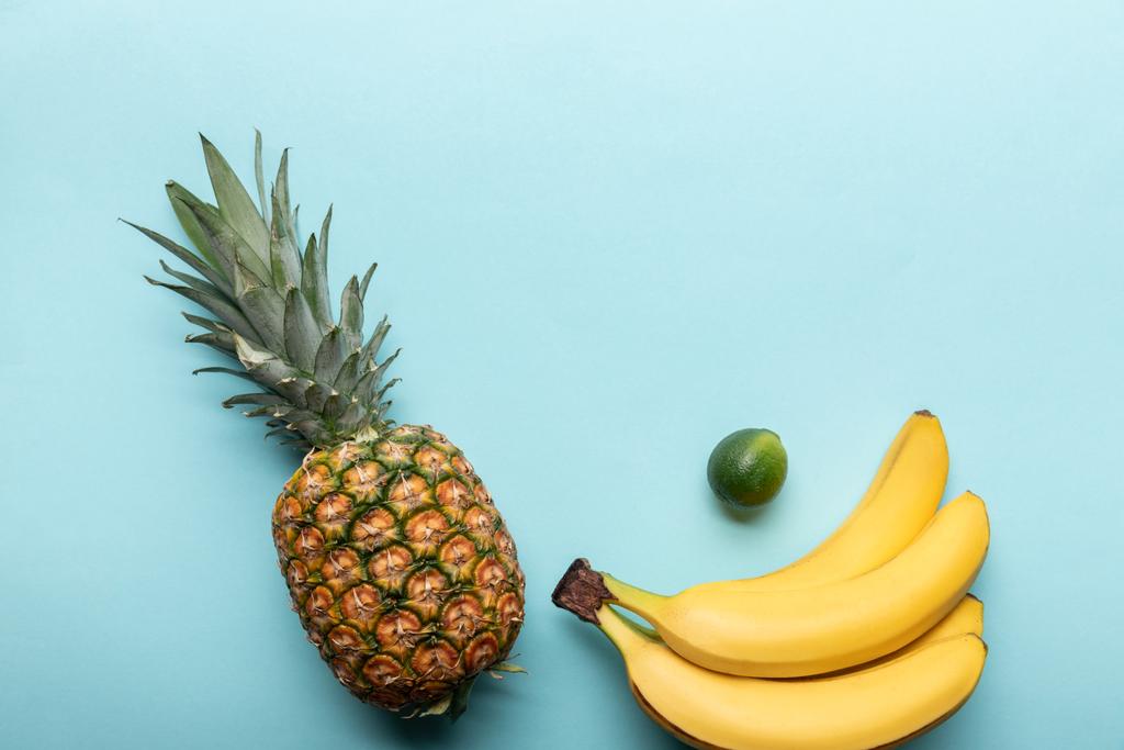 Κορυφαία όψη ολόκληρου ώριμου ανανά, μπανάνας και λάιμ σε μπλε φόντο με χώρο αντιγραφής - Φωτογραφία, εικόνα