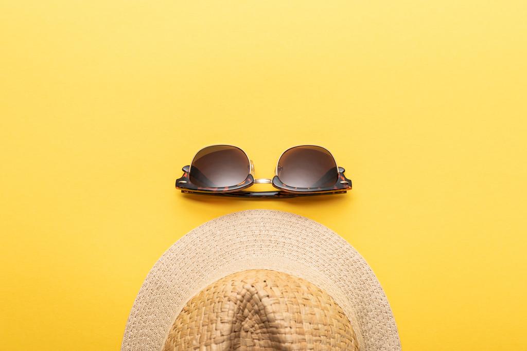 黄色の背景にわら夏の帽子とサングラスのトップビュー - 写真・画像