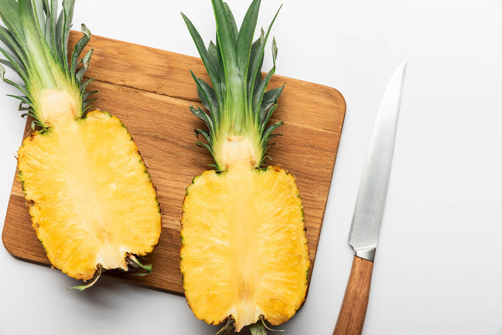 Draufsicht auf geschnittene reife Ananas auf Holzschneidebrett mit Messer auf weißem Hintergrund - Foto, Bild