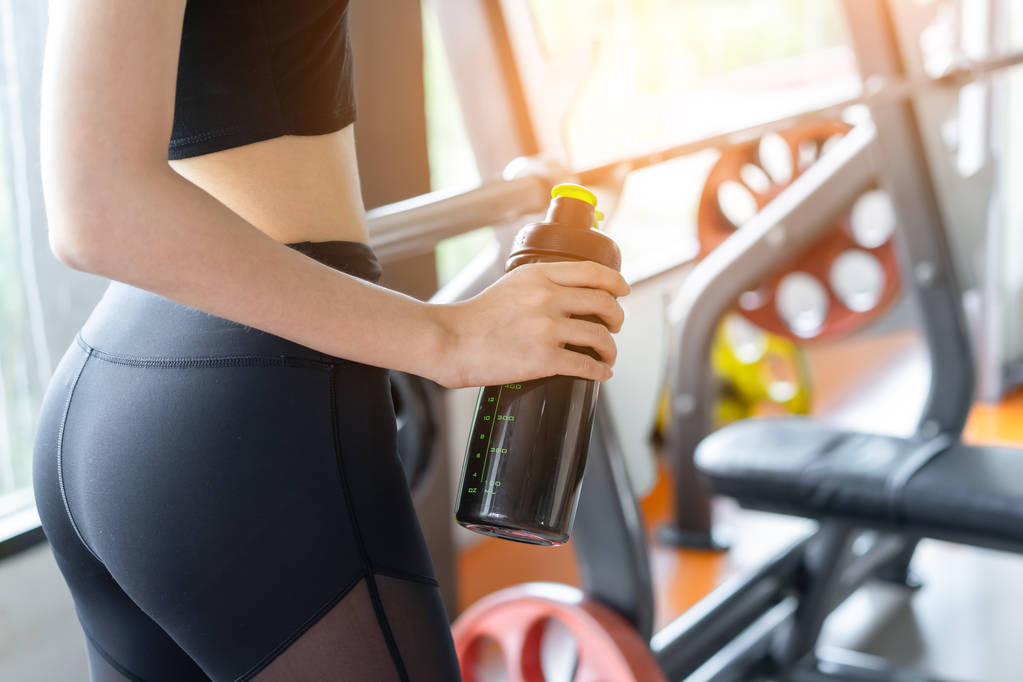 Closeup athlete woman holding whey protein shake bottle at fitness gym after training exercise and workout for building muscle healthy lifestyle relaxation. - Photo, Image