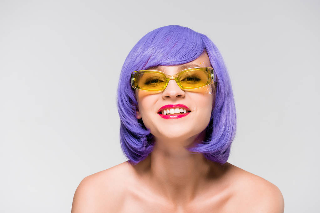 piękna uśmiechnięta dziewczyna w fioletowej peruce i modne okulary przeciwsłoneczne na szarym tle - Zdjęcie, obraz