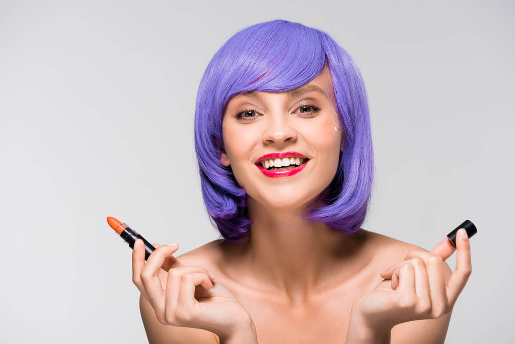 hermosa chica en púrpura peluca celebración de lápiz labial aislado en gris
 - Foto, Imagen