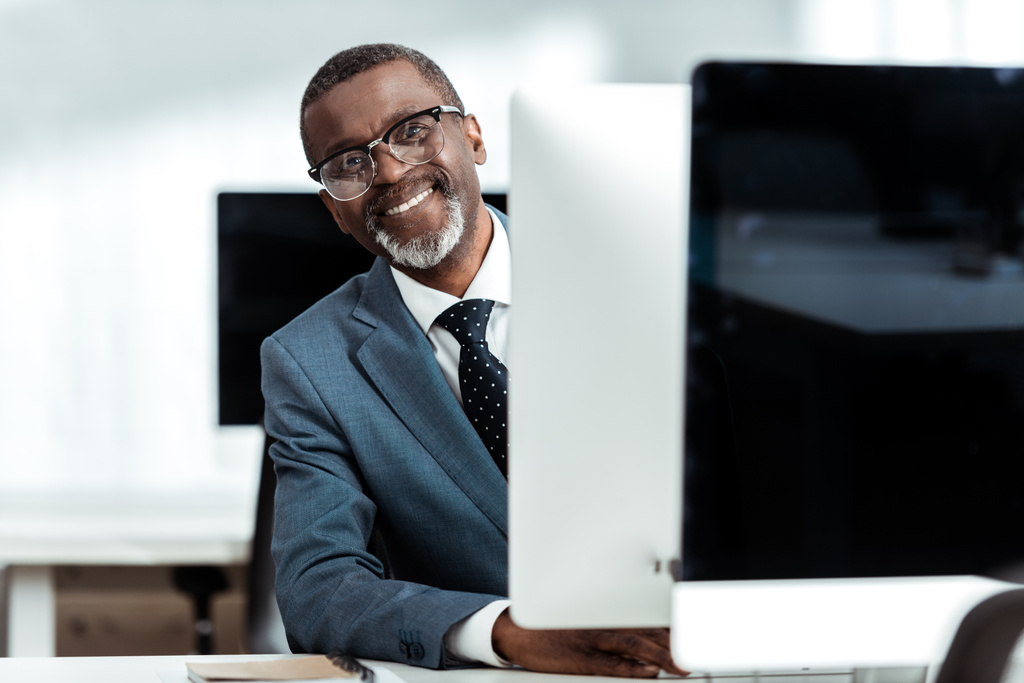 ευτυχισμένος Αφρικανός Αμερικανός επιχειρηματίας με γυαλιά χαμογελώντας στο γραφείο  - Φωτογραφία, εικόνα