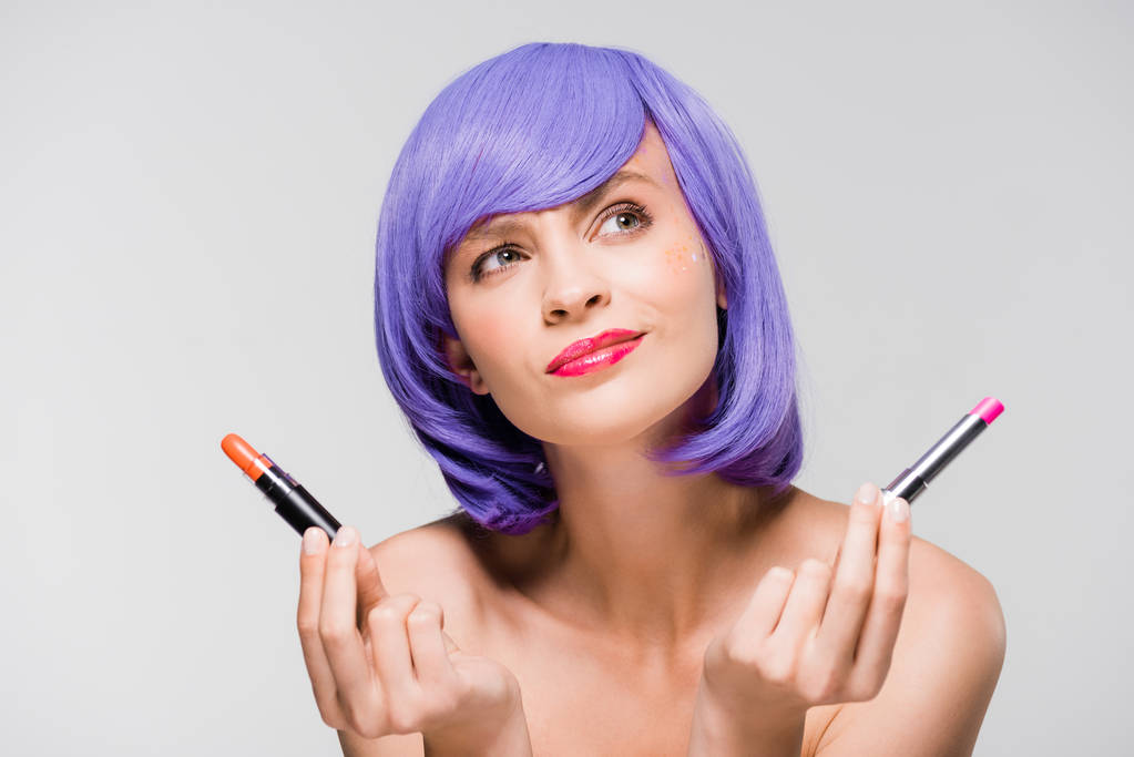 atractiva chica reflexiva en peluca púrpura celebración de lápiz labial aislado en gris
 - Foto, Imagen