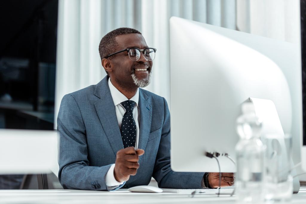 pohled na nízký úhel pohledu na šťastného afroamerického podnikatele, který se dívá na počítačový monitor v kanceláři  - Fotografie, Obrázek