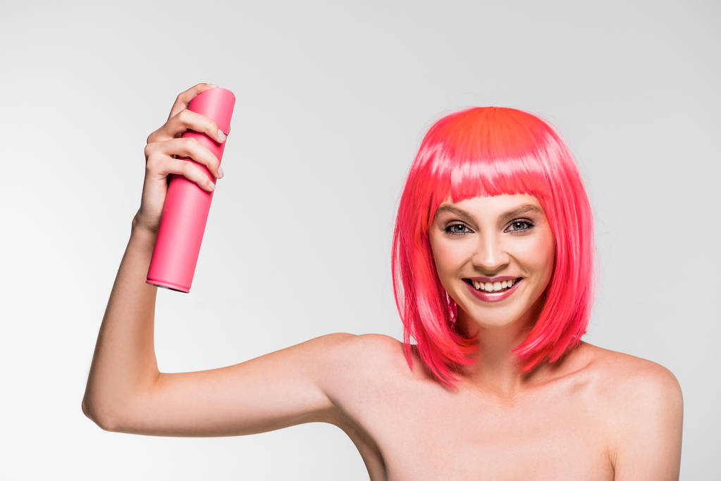 mulher sorridente em peruca rosa segurando spray de cabelo, isolado em cinza
 - Foto, Imagem