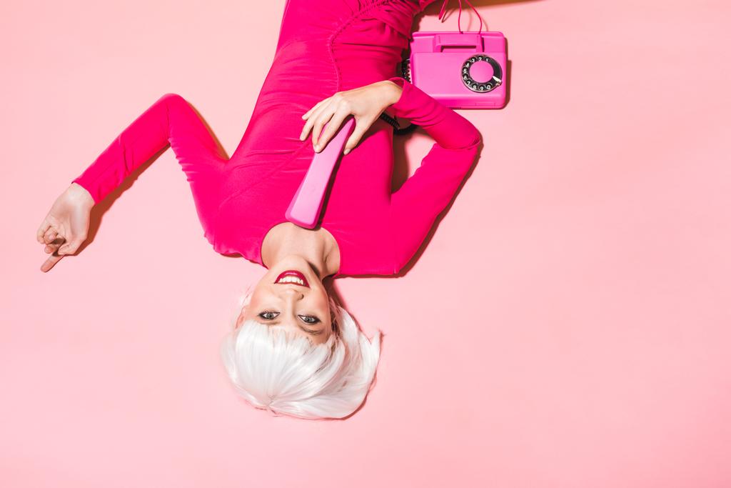 Draufsicht auf stilvolle Frau in weißer Perücke mit Retro-Telefon isoliert auf rosa  - Foto, Bild