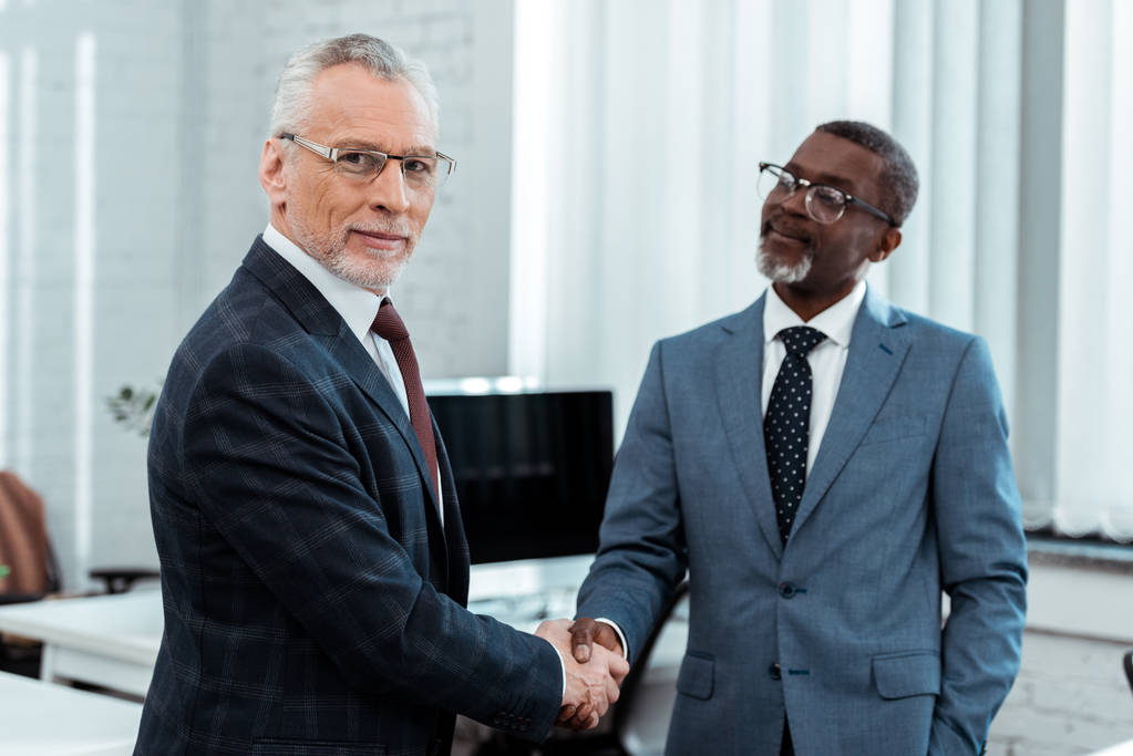 selective focus of happy businessman in glasses shaking hands with african american partner  - Photo, Image